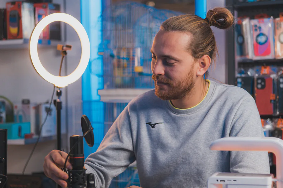 A man looking down at his equipment instead of the camera, with a ring light behind him