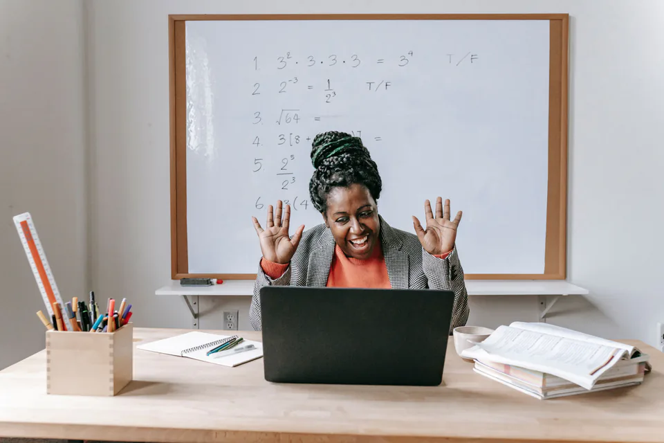 A teacher at a laptop in front of a whiteboard, recording an online lesson
