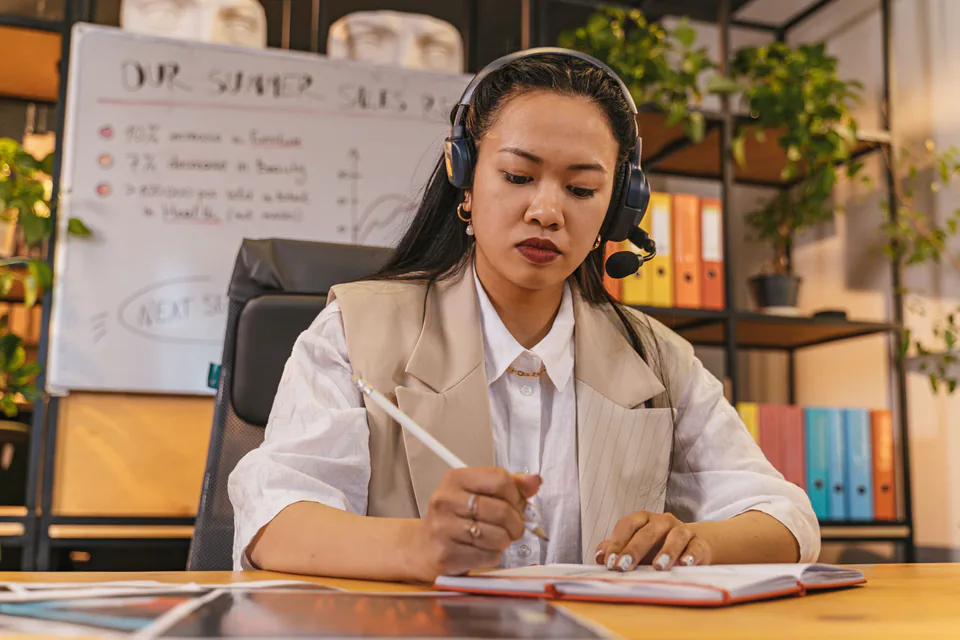 A sales professional wearing a headset and taking notes at a desk